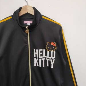 May include: Black track jacket with yellow stripes down the sleeves and a white "HELLO KITTY" logo with a cartoon image of Hello Kitty.