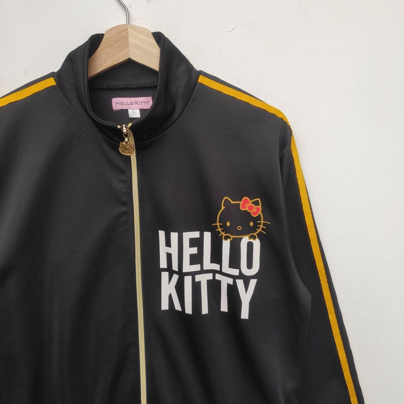 May include: Black track jacket with yellow stripes down the sleeves and a white "HELLO KITTY" logo with a cartoon image of Hello Kitty.