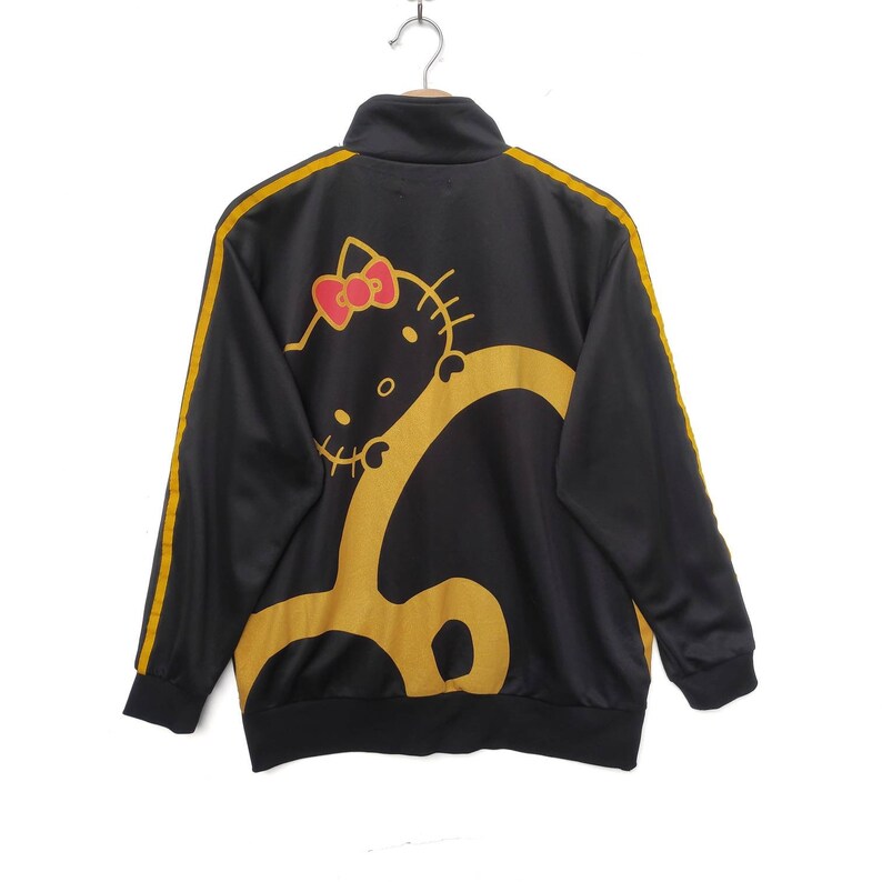 May include: Black track jacket with yellow stripes and a Hello Kitty graphic on the back. The graphic is yellow and red.