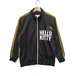 May include: Black track jacket with gold stripes down the sleeves and a Hello Kitty graphic on the front. The zipper is gold.