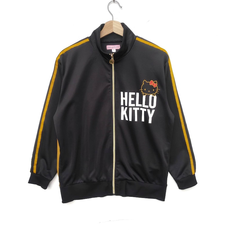 May include: Black track jacket with gold stripes down the sleeves and a Hello Kitty graphic on the front. The zipper is gold.