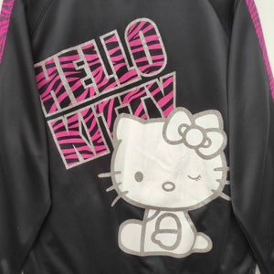 May include: Black zippered jacket with a pink and black zebra print design that says "Hello Kitty" and a white Hello Kitty graphic.