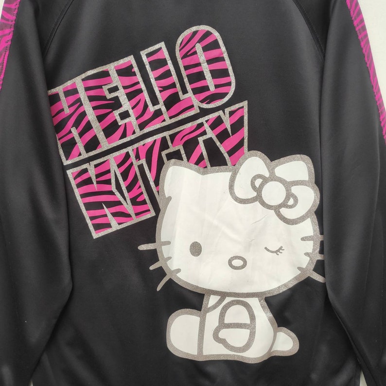 May include: Black zippered jacket with a pink and black zebra print design that says "Hello Kitty" and a white Hello Kitty graphic.