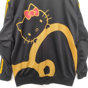 May include: Black zip-up jacket with yellow stripes down the sleeves and a gold Hello Kitty graphic on the back.