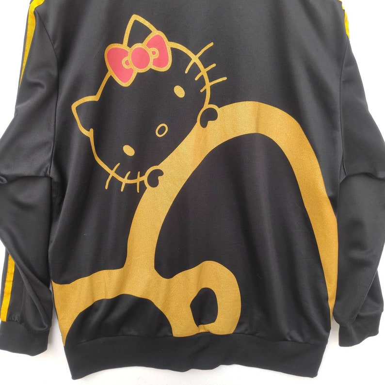 May include: Black zip-up jacket with yellow stripes down the sleeves and a gold Hello Kitty graphic on the back.