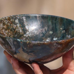 May include: A decorative bowl crafted from polished agate stone. The bowl features a distinctive swirling pattern in shades of brown, green, and white.
