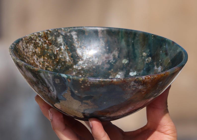 May include: A decorative bowl crafted from polished agate stone. The bowl features a distinctive swirling pattern in shades of brown, green, and white.