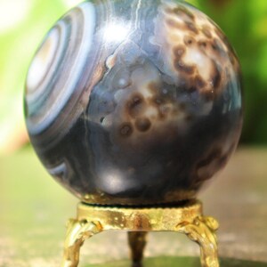 May include: A polished black agate sphere with white and brown banding and a gold metal stand with three legs.