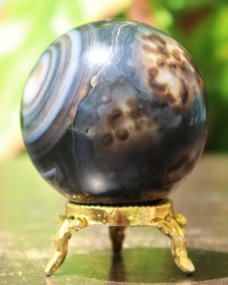 May include: A polished black agate sphere with white and brown banding and a gold metal stand with three legs.