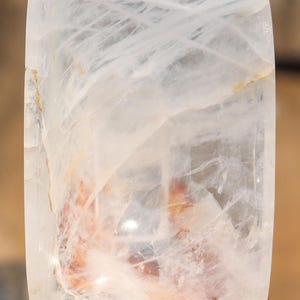 May include: A large, clear quartz crystal bowl with a smooth, polished surface. The bowl is rectangular in shape and has a slightly curved edge. The crystal is translucent and has a slight milky white hue.