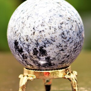 May include: A white and black speckled sphere on a gold metal stand with three legs. The sphere is made of polished stone.