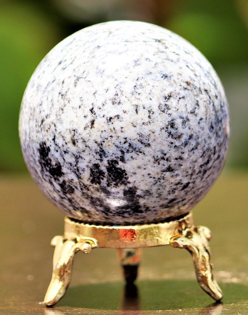 May include: A white and black speckled sphere on a gold metal stand with three legs. The sphere is made of polished stone.