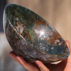 May include: A large, green, brown, and white agate bowl. The bowl is carved from a single piece of agate and has a natural, organic shape.