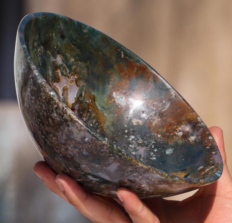 May include: A large, green, brown, and white agate bowl. The bowl is carved from a single piece of agate and has a natural, organic shape.