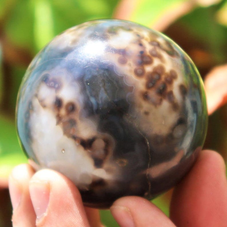 May include: A polished agate sphere with a swirling pattern of black, white, and brown. The sphere is smooth and has a high gloss finish.
