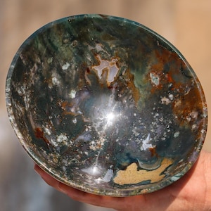 May include: A green, brown and white agate bowl with a swirling pattern. The bowl is polished and has a shiny finish.