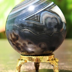 May include: A black and white agate sphere on a gold metal stand. The sphere has a swirling pattern of black, white, and gray bands.