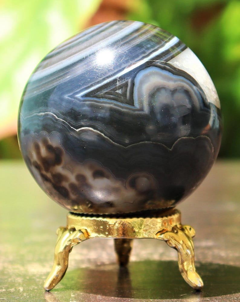 May include: A black and white agate sphere on a gold metal stand. The sphere has a swirling pattern of black, white, and gray bands.