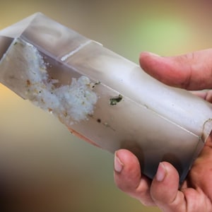 May include: A clear, translucent crystal with a gray and white cloudy pattern. The crystal is shaped like a long, pointed prism.