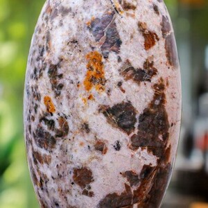 May include: A large, oval-shaped, polished stone with a white, brown, and orange marbled pattern. The stone is sitting on a wooden base.