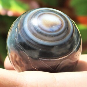 May include: A polished black and white agate sphere with concentric rings. The sphere is smooth and has a high gloss finish.