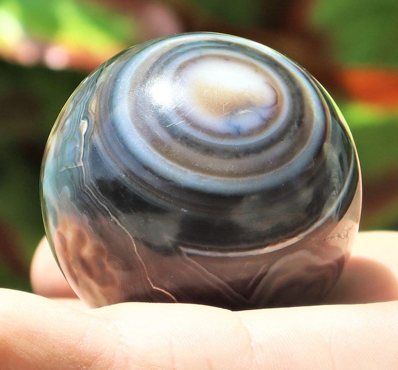 May include: A polished black and white agate sphere with concentric rings. The sphere is smooth and has a high gloss finish.