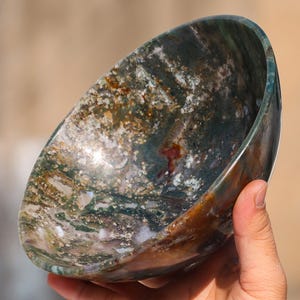 May include: A large, round bowl made of green, brown, and white agate. The bowl has a natural, polished finish and is perfect for decorative purposes.