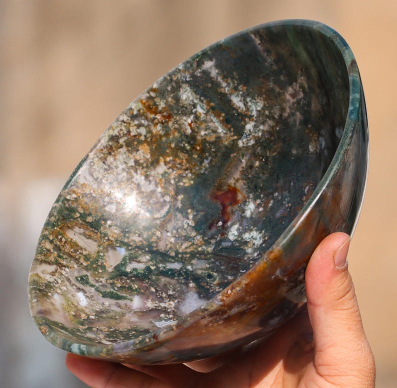May include: A large, round bowl made of green, brown, and white agate. The bowl has a natural, polished finish and is perfect for decorative purposes.