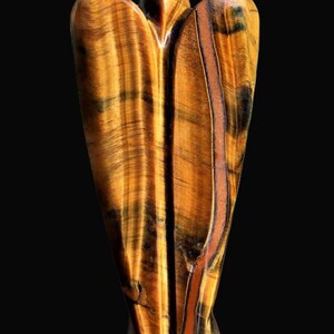 Peut inclure: Une figurine d'ange en pierre d'&oelig;il de tigre sculpt&eacute;e. La sculpture pr&eacute;sente une palette chaleureuse de teintes brun dor&eacute; avec des stries brun fonc&eacute; et noires. L'ange a une finition lisse et polie, sur fond noir.