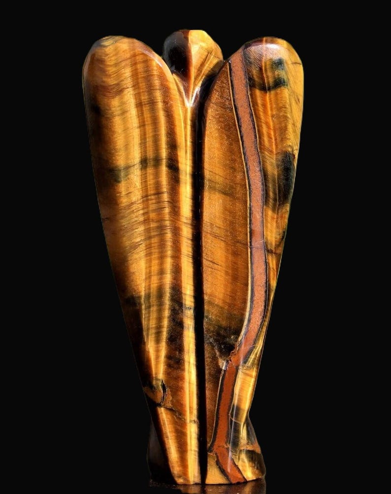 Peut inclure: Une figurine d'ange en pierre d'&oelig;il de tigre sculpt&eacute;e. La sculpture pr&eacute;sente une palette chaleureuse de teintes brun dor&eacute; avec des stries brun fonc&eacute; et noires. L'ange a une finition lisse et polie, sur fond noir.