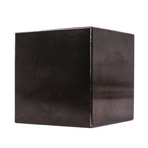 Puede incluir: Un cubo geométrico sólido con un acabado negro oscuro y liso. El objeto presenta bordes afilados y limpios con lados planos y uniformes, mostrando una forma cuadrada tridimensional simple que refleja la luz sobre su superficie pulida.