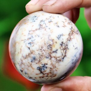 May include: A white, round, polished stone sphere with brown and black markings. The sphere is about the size of a baseball.
