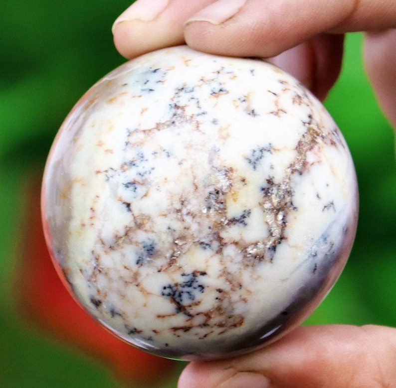 May include: A white, round, polished stone sphere with brown and black markings. The sphere is about the size of a baseball.