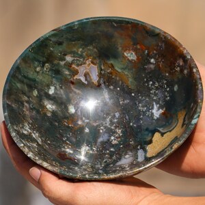 May include: A green, brown, and white agate bowl with a polished finish. The bowl is round and has a slight curve to the sides. The bowl is made of natural stone and has a unique pattern.