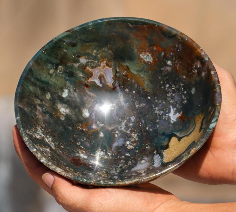 May include: A green, brown, and white agate bowl with a polished finish. The bowl is round and has a slight curve to the sides. The bowl is made of natural stone and has a unique pattern.