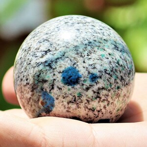 May include: A smooth, white sphere with blue and black flecks. The sphere is made of a natural stone, possibly granite or marble.