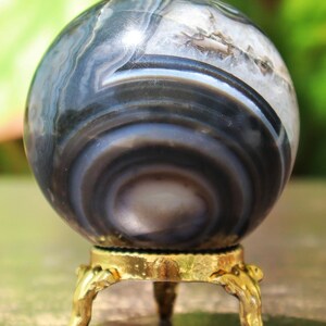 May include: A polished agate sphere with a swirling pattern of black and white bands, displayed on a gold metal stand with three legs.