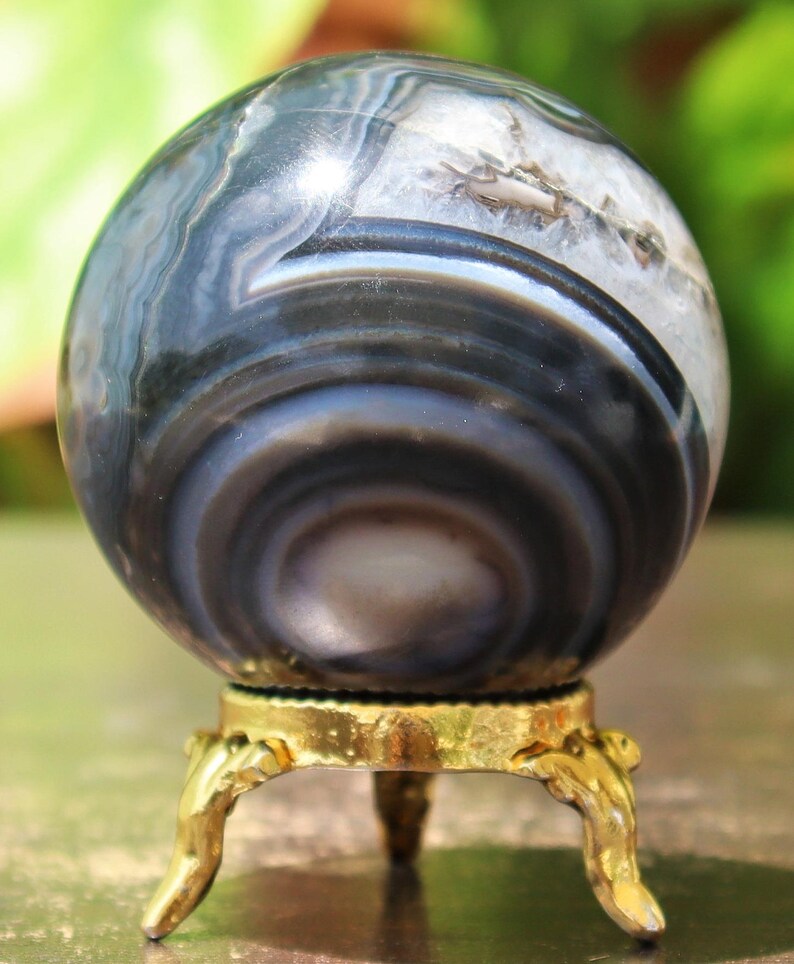 May include: A polished agate sphere with a swirling pattern of black and white bands, displayed on a gold metal stand with three legs.