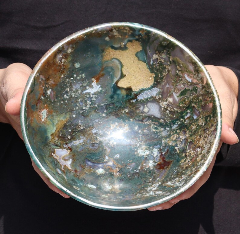 May include: A large, round bowl made of polished green, brown, and white agate. The bowl has a natural, organic pattern and a smooth, shiny surface.