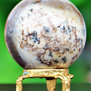May include: A white and brown agate sphere on a gold metal stand with three legs. The sphere has a swirling pattern of white, brown, and black.