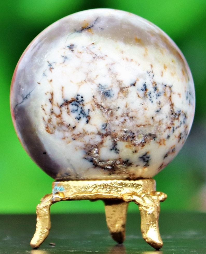 May include: A white and brown agate sphere on a gold metal stand with three legs. The sphere has a swirling pattern of white, brown, and black.