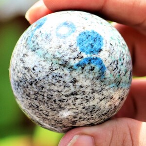 May include: A smooth, round, polished sphere of blue kyanite embedded in a white and gray granite matrix.
