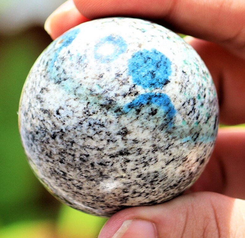 May include: A smooth, round, polished sphere of blue kyanite embedded in a white and gray granite matrix.