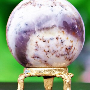 May include: A white and purple agate sphere on a gold metal stand with three legs. The sphere has brown and white markings.