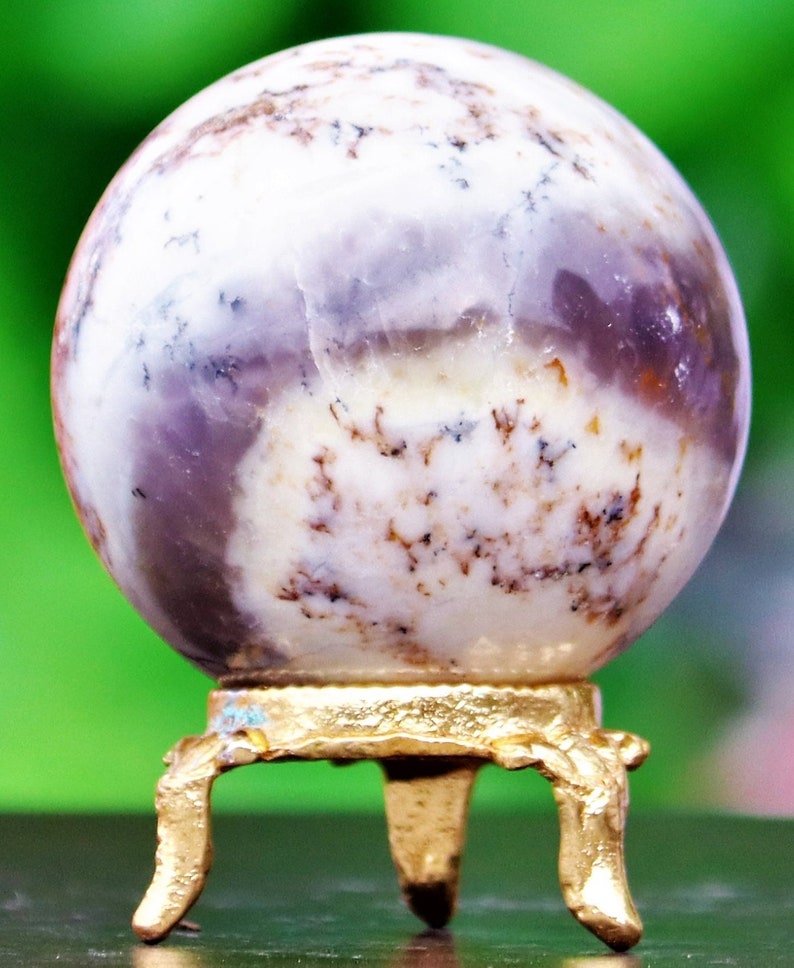 May include: A white and purple agate sphere on a gold metal stand with three legs. The sphere has brown and white markings.