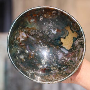 May include: A green, brown and white agate bowl with a swirling pattern. The bowl is made of natural stone and has a smooth, polished finish.
