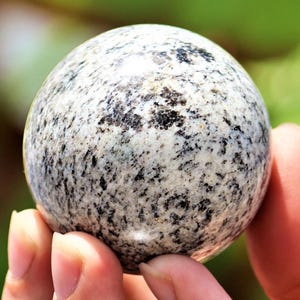 May include: A polished sphere of granite with a white and black speckled pattern. The sphere is smooth and has a glossy finish.
