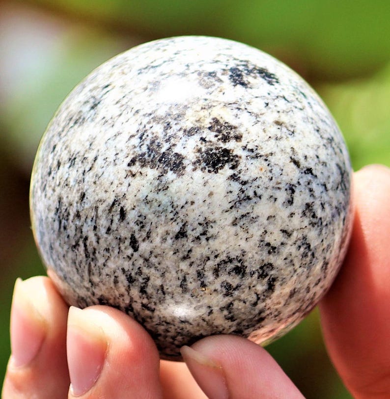 May include: A polished sphere of granite with a white and black speckled pattern. The sphere is smooth and has a glossy finish.
