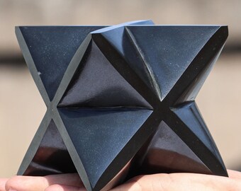 May include: A black obsidian star shaped crystal, carved from a single piece of obsidian. The crystal is smooth and polished, with a high gloss finish. The star is a geometric shape with five points.