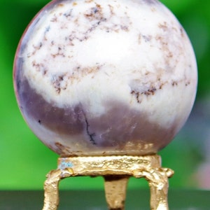 May include: A white and purple agate sphere on a gold metal stand with three legs. The sphere has a swirling pattern of white, purple, and brown.